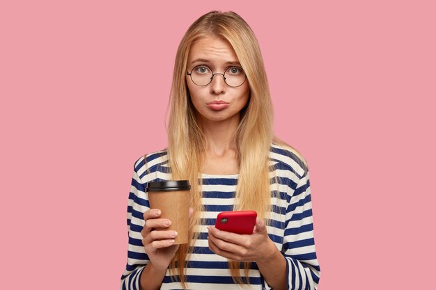 Femme blonde triste avec une expression offensive, serre les lèvres de mécontentement comme reçoit un mauvais message