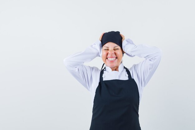 Femme blonde en uniforme de cuisinier noir en appuyant sur les mains sur l'oreille, fermant les yeux et à la jolie