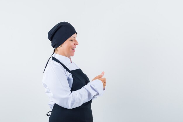 Femme blonde en uniforme de cuisinier noir qui s'étend et se frotte les mains et à la jolie