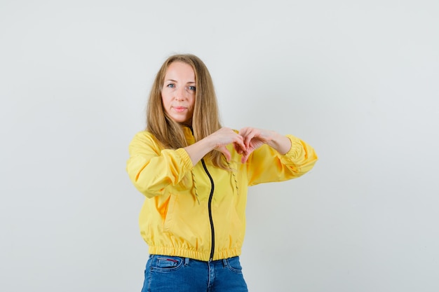 Femme blonde en veste, jeans montrant le geste du cœur et à la jolly,