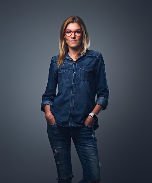 Photo gratuite femme blonde vêtue d'une chemise en jean et de lunettes rouges posant sur fond gris.