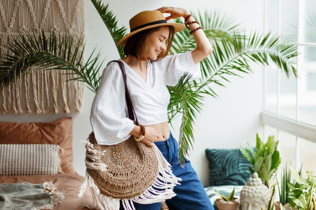 Femme bohème ludique posant dans une chambre élégante avec un intérieur incroyable, des palmiers et du macramé