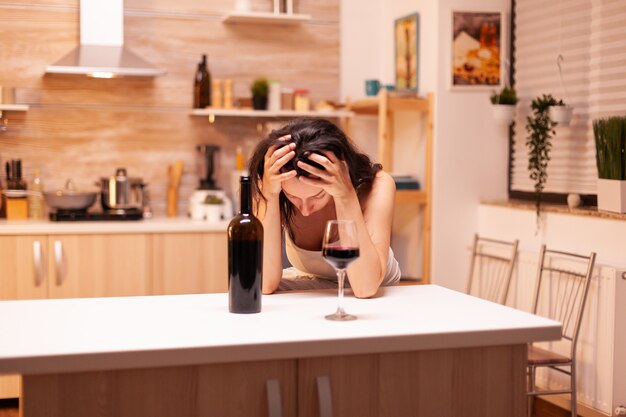 Une femme avec une boisson alcoolisée boit seule une bouteille de vin qui lui donne la gueule de bois