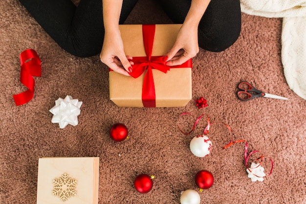 Femme avec une boîte de cadeau près des arcs, des boules de Noël et des ciseaux