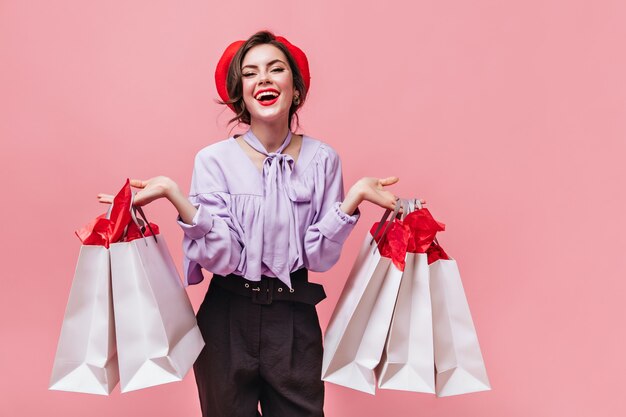 Une femme de bonne humeur rit et tient des paquets après avoir fait du shopping sur fond rose.