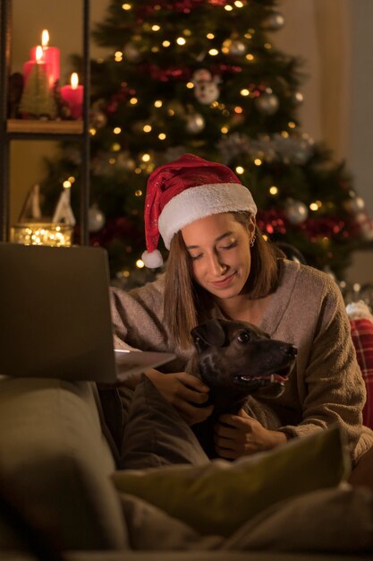 Femme avec bonnet de Noel tenant un chien à côté de l'ordinateur portable