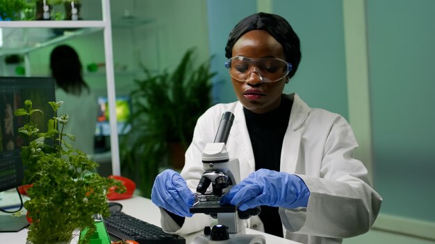 Femme botaniste regardant l'échantillon d'essai au microscope observant la mutation génétique sur les plantes