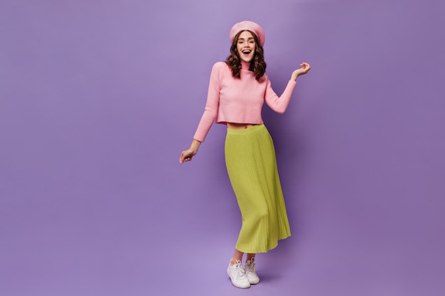 Une femme bouclée assez heureuse danse sur un mur violet