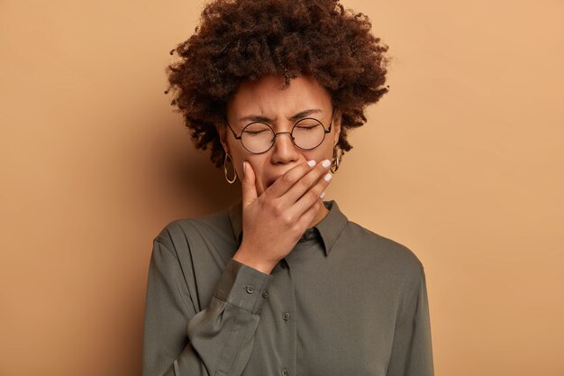 Femme bouclée endormie bâille les yeux fermés, couvre la bouche, est fatiguée, manque de sommeil et d'énergie, a besoin de repos, souffre d'insomnie