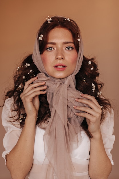 Femme bouclée avec des fleurs dans ses cheveux, attachant l'écharpe à l'arc et regardant la caméra.