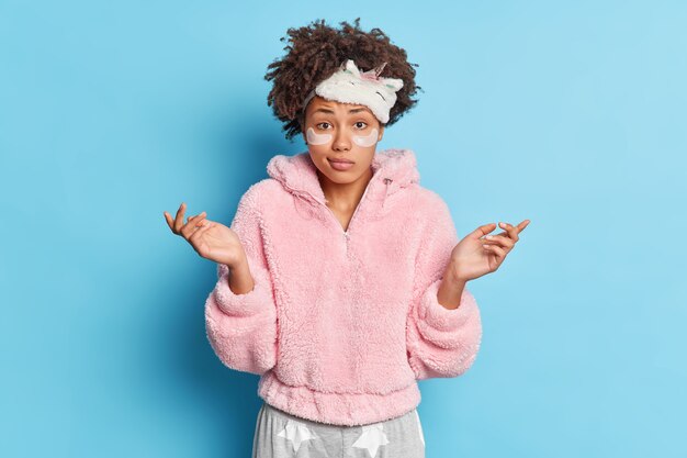 Femme bouclée à la peau sombre confuse étend les paumes avec une expression hésitante