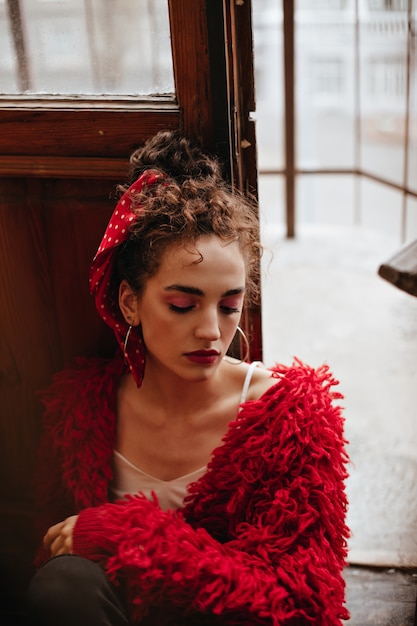 Photo gratuite femme bouclée en pull rouge pose près de la porte en bois