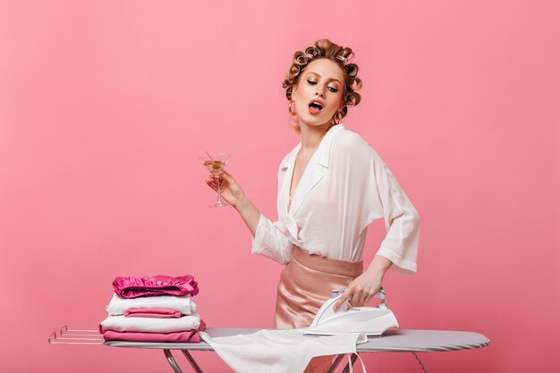 Femme avec des boucles vêtues de vêtements élégants tenant le verre à martini et le linge à repasser