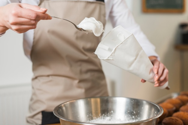 Femme boulanger remplissant la crème fouettée dans le sac à glaçage blanc
