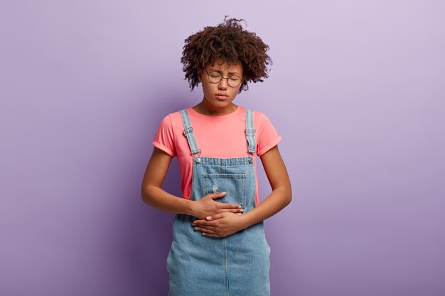 Une femme bouleversée garde les mains sur le ventre, souffre de douleurs menstruelles, de crampes et de maux d'estomac, a une gastrite chronique, des maux d'estomac