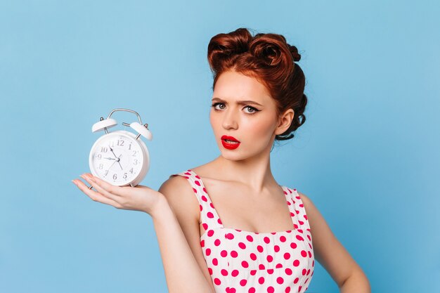 Femme bouleversée avec un maquillage lumineux montrant l'heure. Photo de Studio de belle pin-up avec horloge.