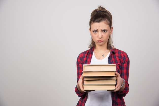 Une femme bouleversée montrant une pile de livres sur un mur gris