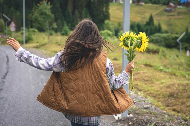 Femme avec un bouquet de tournesols dans la nature dans une région montagneuse