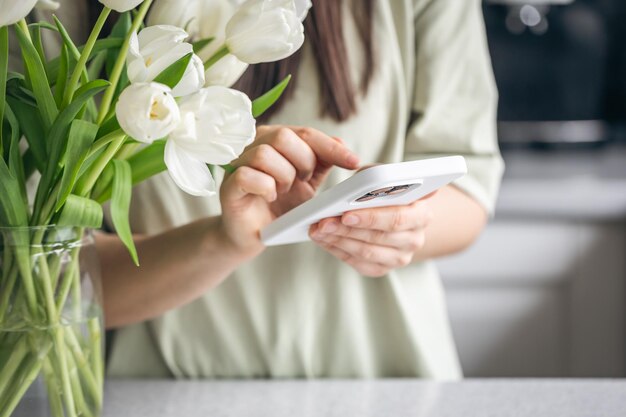 Photo gratuite une femme avec un bouquet de tulipes blanches utilise un gros plan de son smartphone