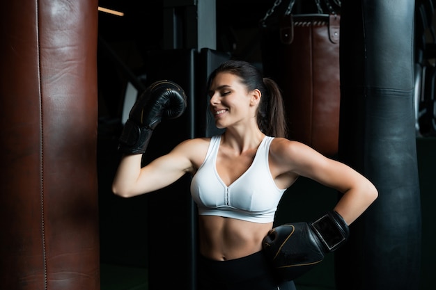 Femme de boxe posant avec un sac de boxe, sur une salle de sport sombre. Concept de femme forte et indépendante