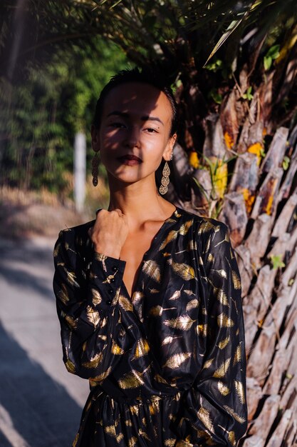 femme avec bronze maquillage en robe dorée noire près d'un palmier