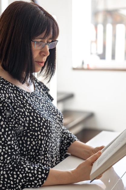 Une femme brune d'âge moyen à lunettes avec une coupe de cheveux bob lit un livre