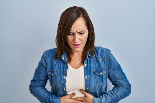 Photo gratuite femme brune d'âge moyen portant une veste en jean décontractée sur fond isolé avec la main sur l'estomac parce que l'indigestion, la maladie douloureuse se sent mal. notion de mal.