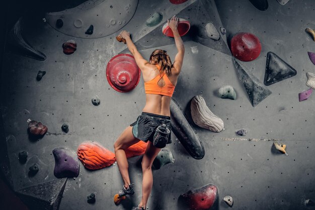 Femme brune athlétique sur un mur d'escalade intérieur.