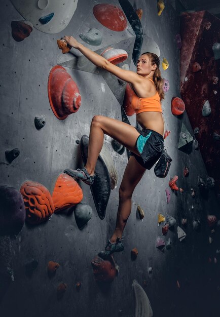 Femme brune athlétique sur un mur d'escalade intérieur.