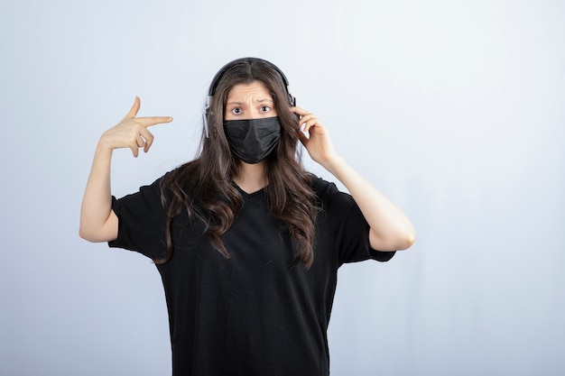 Femme brune aux cheveux longs dans un masque médical pointant sur les écouteurs.