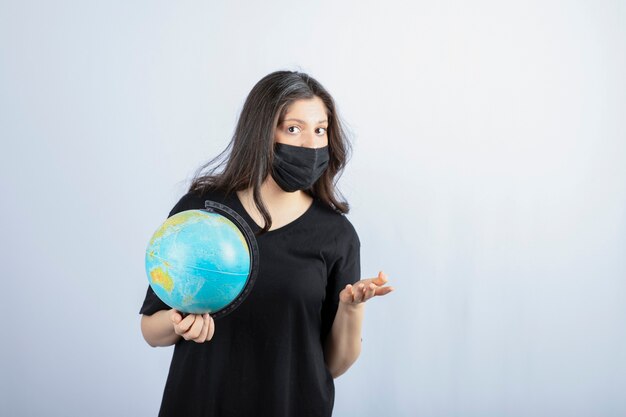 Femme brune aux cheveux longs en masque médical tenant le globe terrestre.