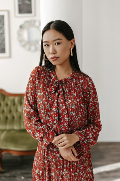 Une femme brune aux yeux bruns en robe rouge à fleurs regarde à l'avant