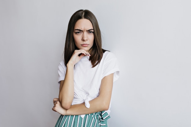 Femme brune concentrée posant. Photo intérieure d'une adorable fille aux cheveux bruns touchant son visage.