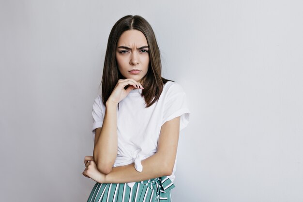 Femme brune concentrée posant. Photo intérieure d'une adorable fille aux cheveux bruns touchant son visage.