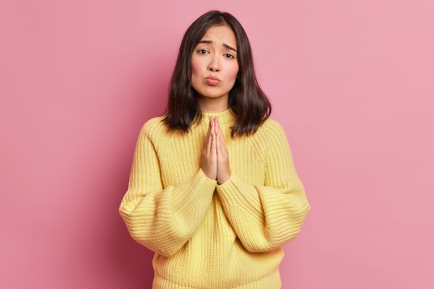 Une femme brune désespérée maintient les paumes pressées l'une contre l'autre et regarde avec une expression implorante demande faveur demande de donner une autre chance porte un pull jaune à manches longues