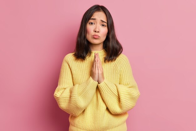 Une femme brune désespérée maintient les paumes pressées l'une contre l'autre et regarde avec une expression implorante demande faveur demande de donner une autre chance porte un pull jaune à manches longues