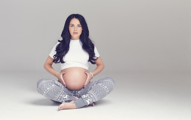 Femme brune enceinte assise avec les jambes croisées.