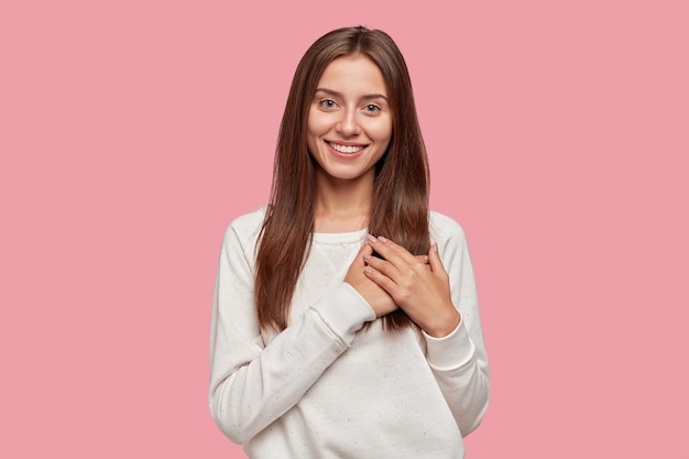 Femme brune généreuse satisfaite avec un sourire tendre, garde les deux paumes sur la poitrine