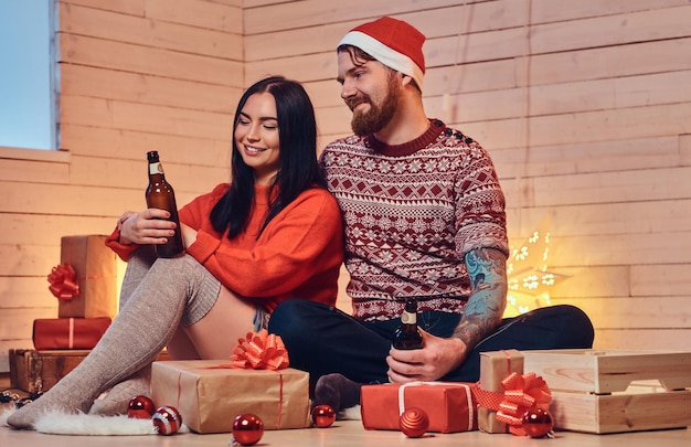 Une femme brune et un hipster barbu boivent de la bière et célèbrent Noël à la maison.