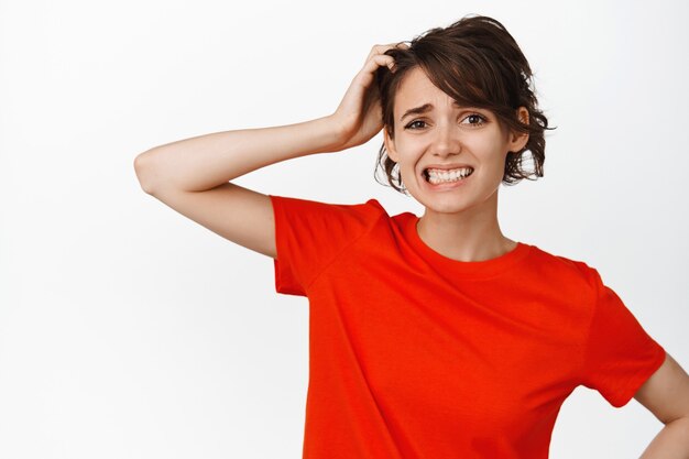 Une femme brune indécise a l'air perplexe, confuse avec smth, se gratte la tête et a l'air perplexe sur le blanc.