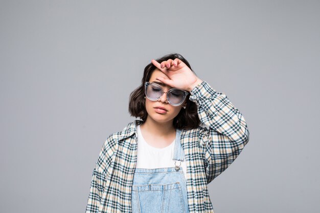 Femme brune de mode en robe et lunettes de soleil posant dans le mur isolé sur blanc