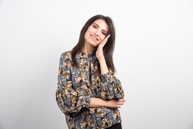 Femme brune posant avec le sourire sur un fond blanc.