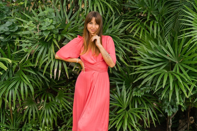 Femme brune romantique en robe rose élégante profitant de vacances tropicales