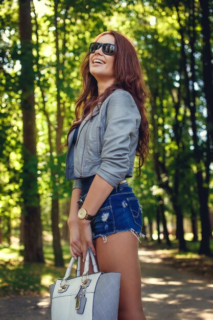 Femme brune en short et veste grise posant dans un parc naturel de printemps.