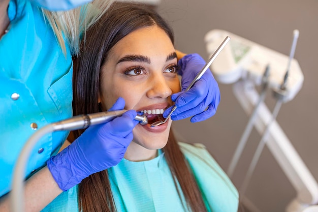 Femme brune souriante examinée par un dentiste à la clinique dentaire. mains d'un médecin tenant des instruments dentaires près de la bouche du patient. dents saines et concept de médecine