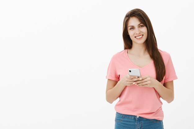 Femme brune souriante posant dans le studio avec son téléphone