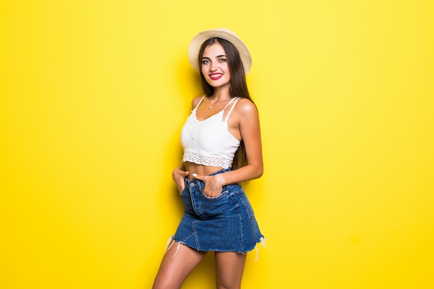 Femme brune souriante en pull posant avec les bras croisés sur le mur jaune