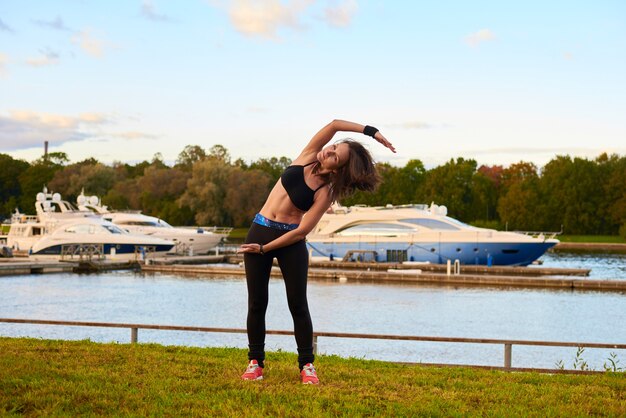 Femme brune de sport heureux en débardeur noir et collants faisant étirement latéral debout. Concept de formation en soirée sur la plage de la vie de la santé.