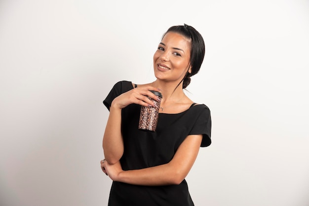 Femme brune avec une tasse de café en riant sur un mur blanc.