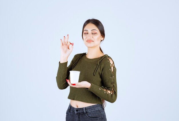 femme brune tenant une tasse en plastique et donnant un signe ok.